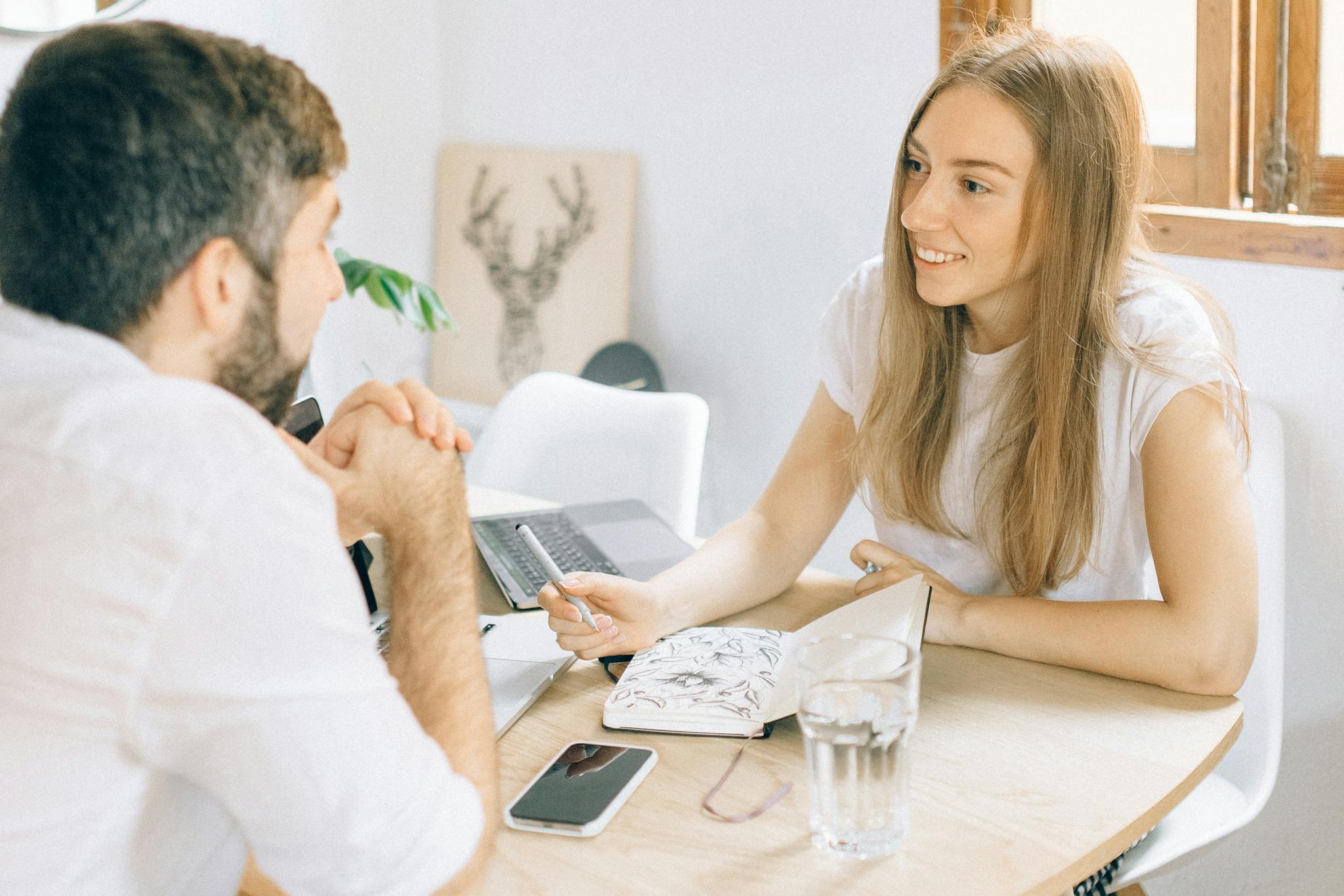 A smiling woman and man having a friendly discussion at a table with a notebook and laptop.