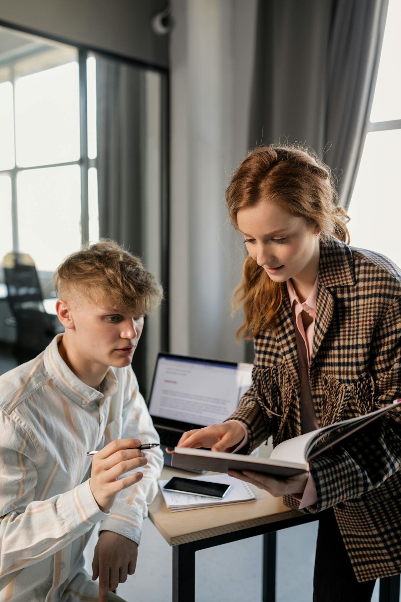 Two young professionals discussing work at a modern office desk.